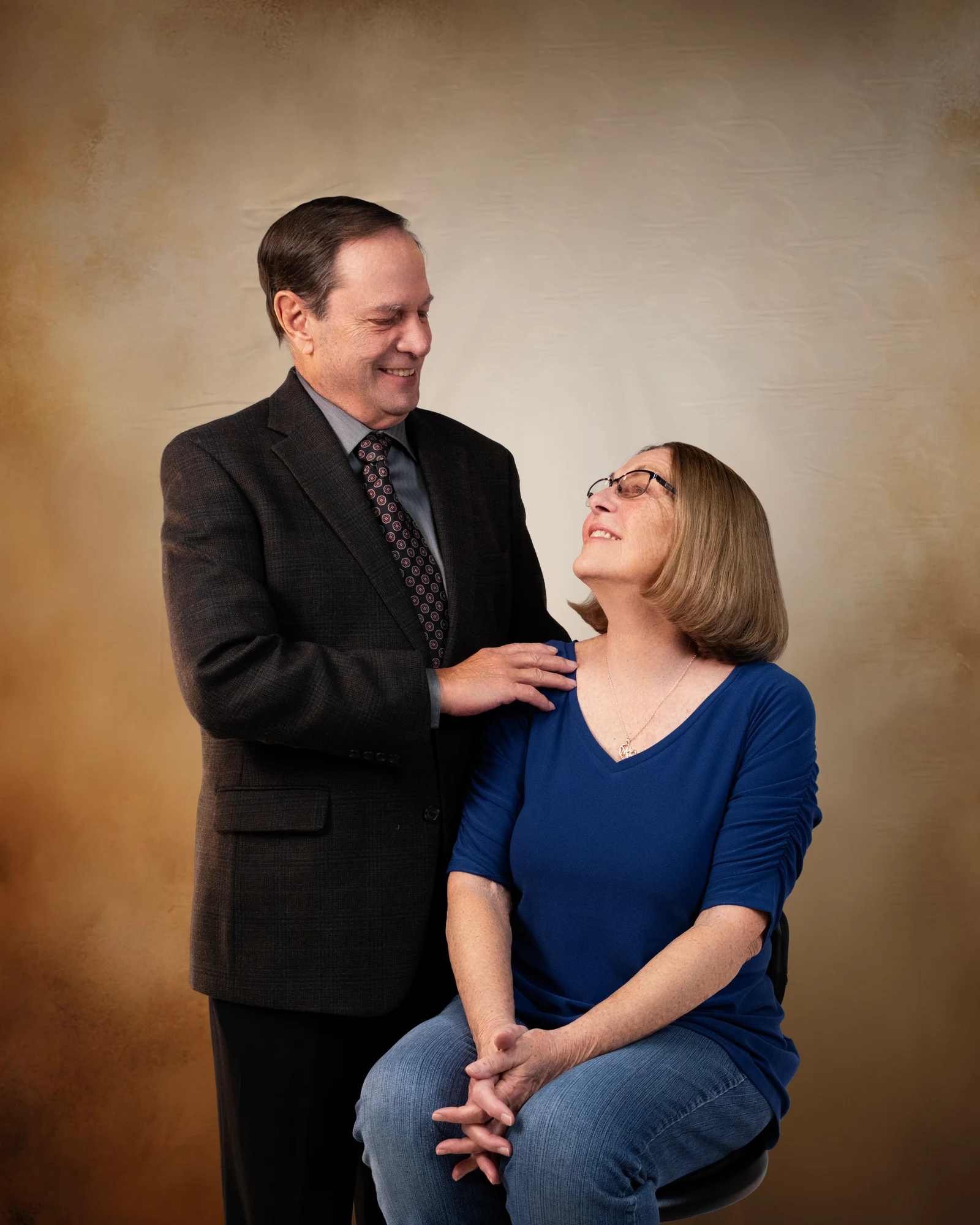 A couple sharing a smile against a warm studio backdrop