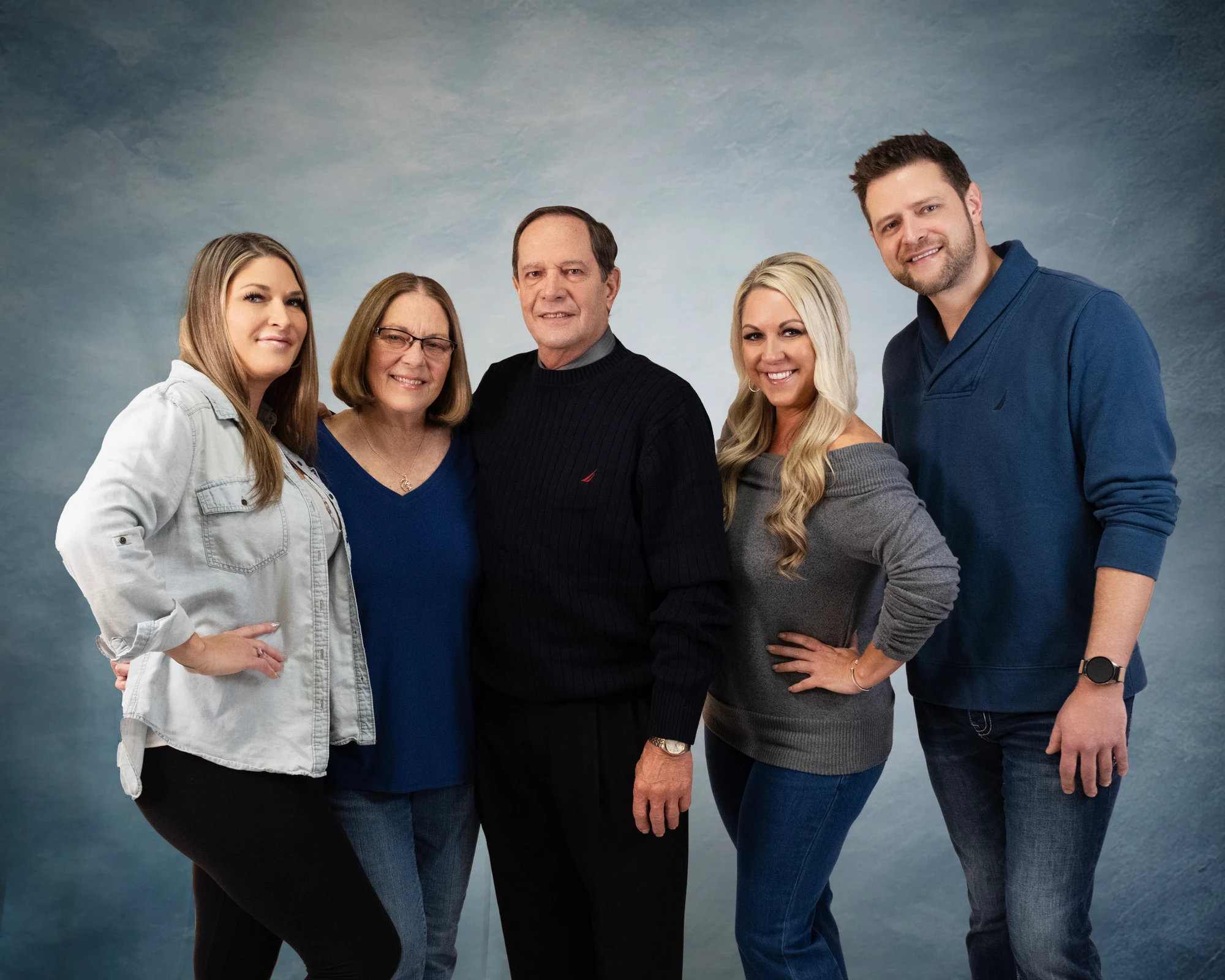 Five family members standing together against a blue studio backdrop