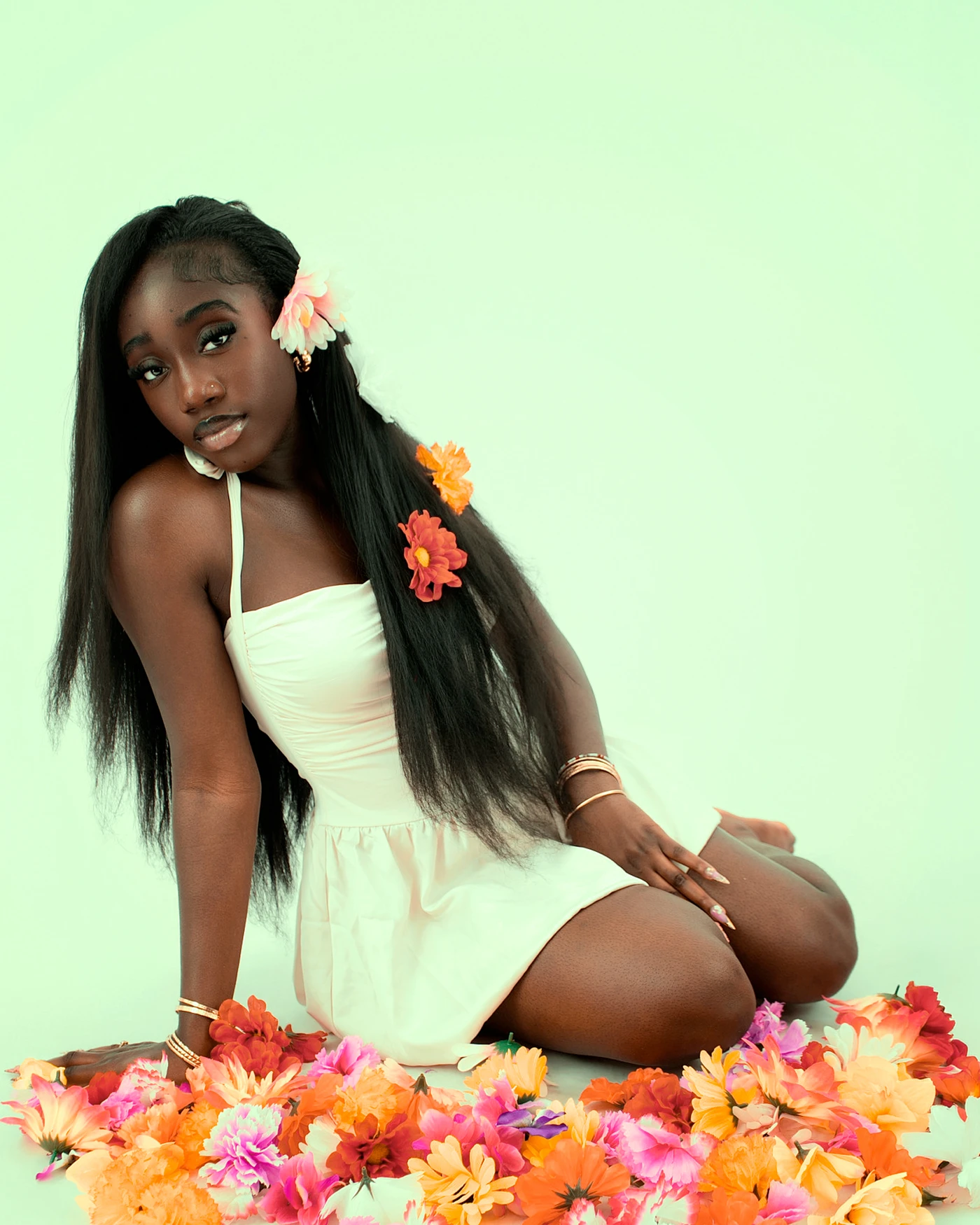A seated portrait in a white dress surrounded by orange and pink flowers
