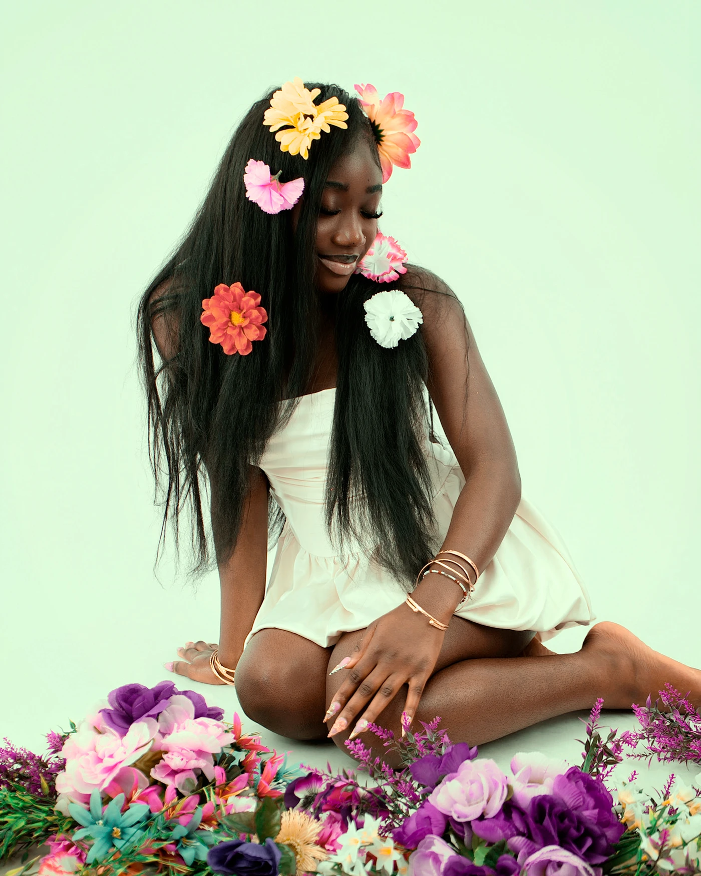 A seated portrait looking down among colorful flowers against a mint backdrop