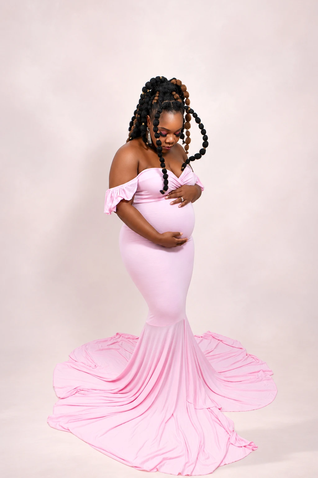 A mother-to-be looking down at her bump in a flowing pink gown