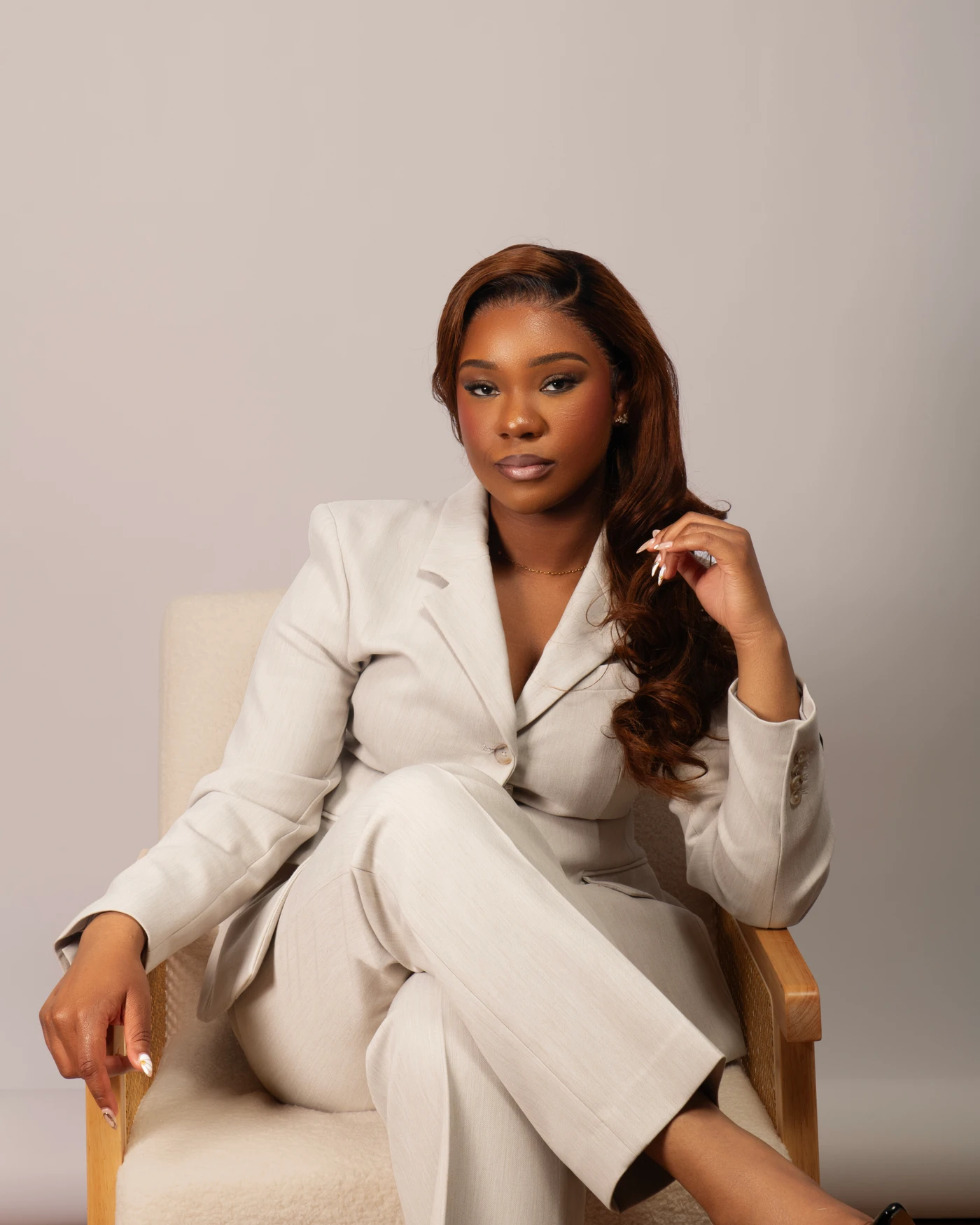 A studio portrait in a cream pantsuit with one hand resting beside her hair