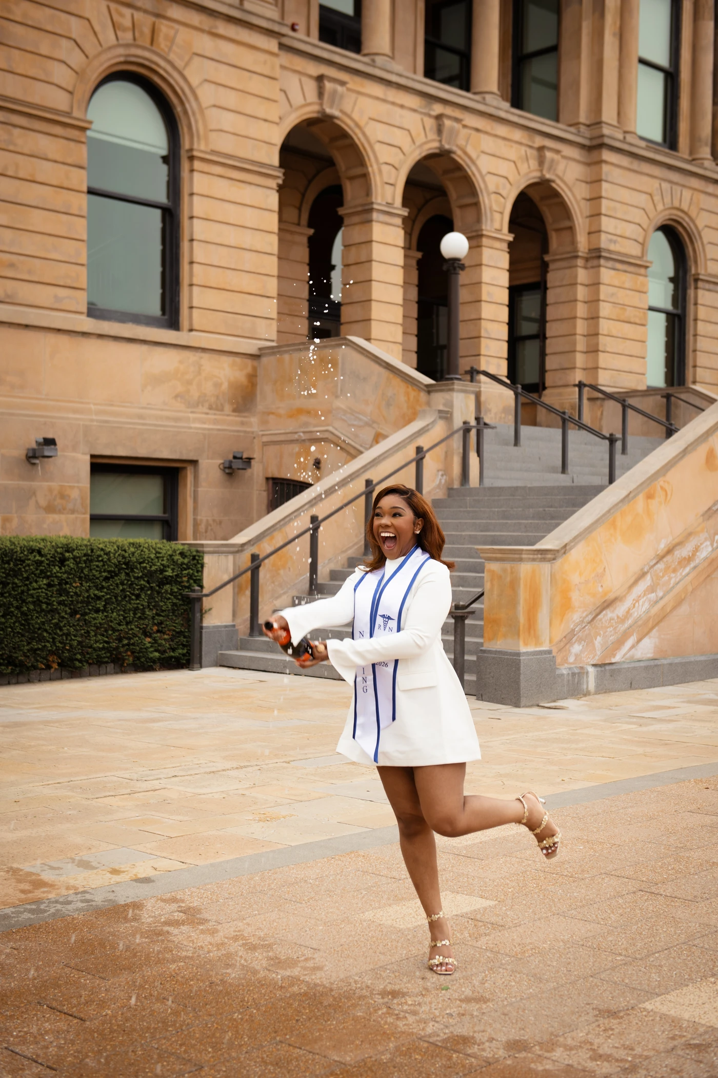 A nursing graduate celebrating with a spray of bubbles outside a stone building