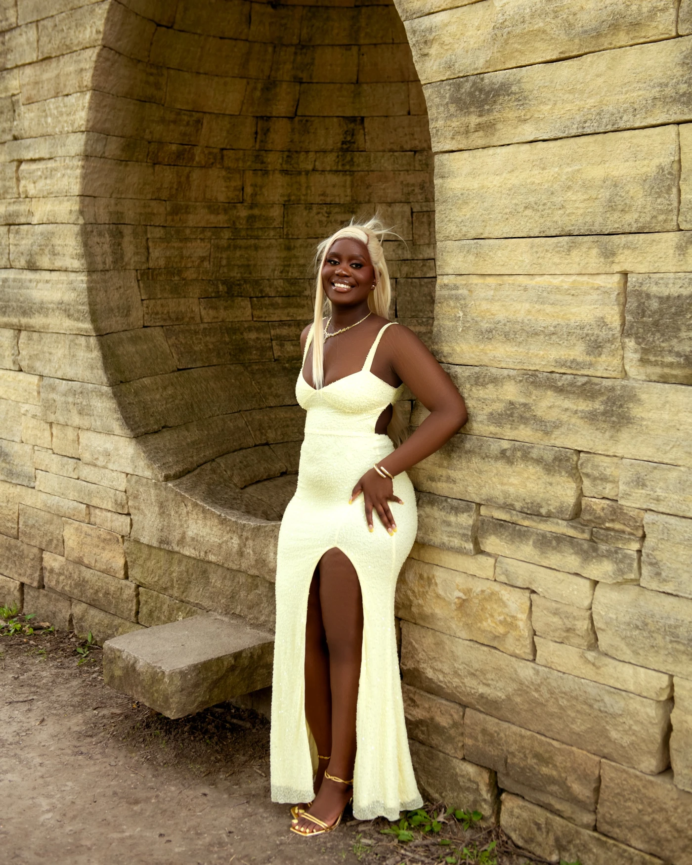 A smiling full-length portrait beside a stone alcove