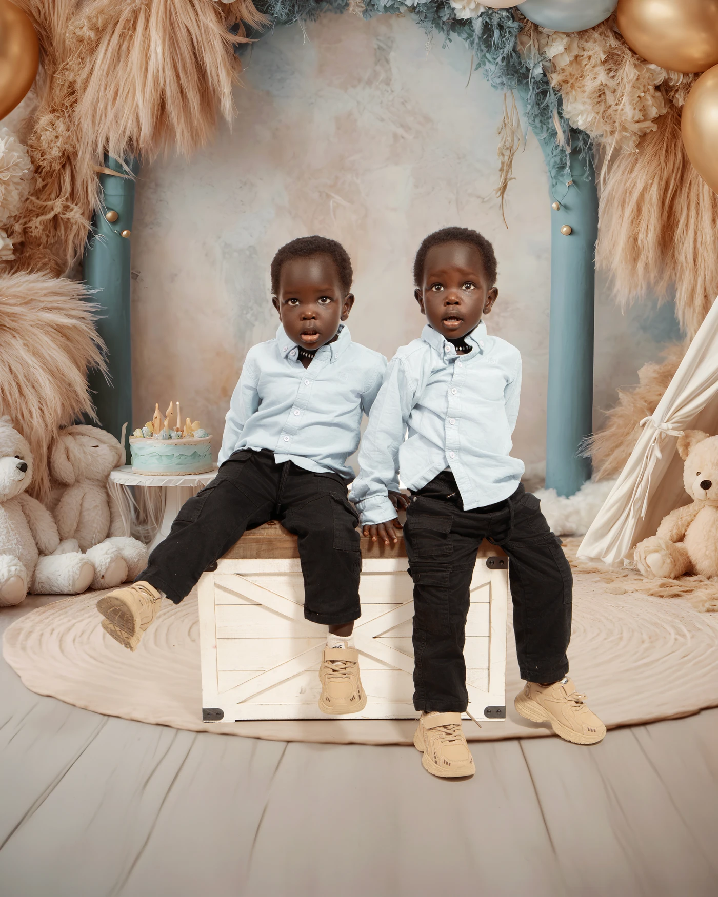 Two children seated together beside a birthday cake and teddy bears