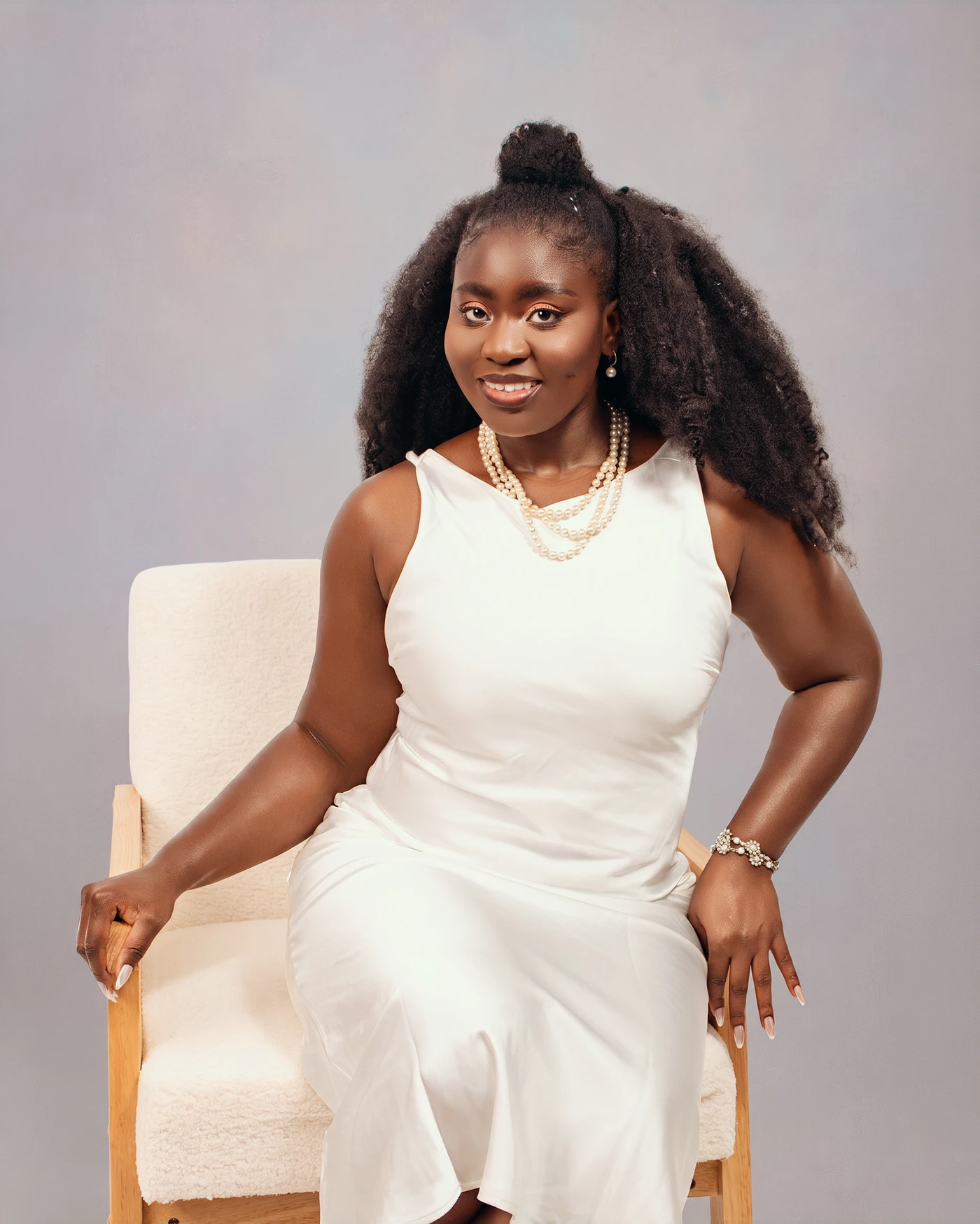 A smiling woman in a white dress seated for a studio portrait