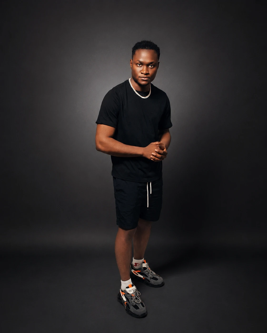 A man in black posing against a dark studio backdrop