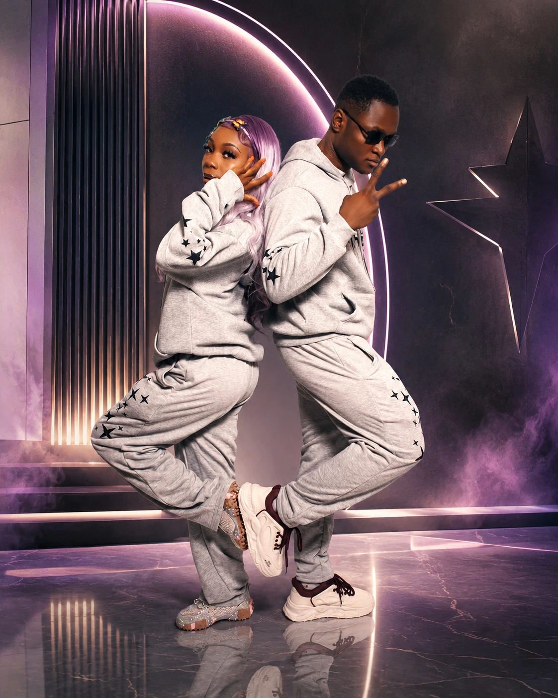 A couple posing back to back in matching gray tracksuits
