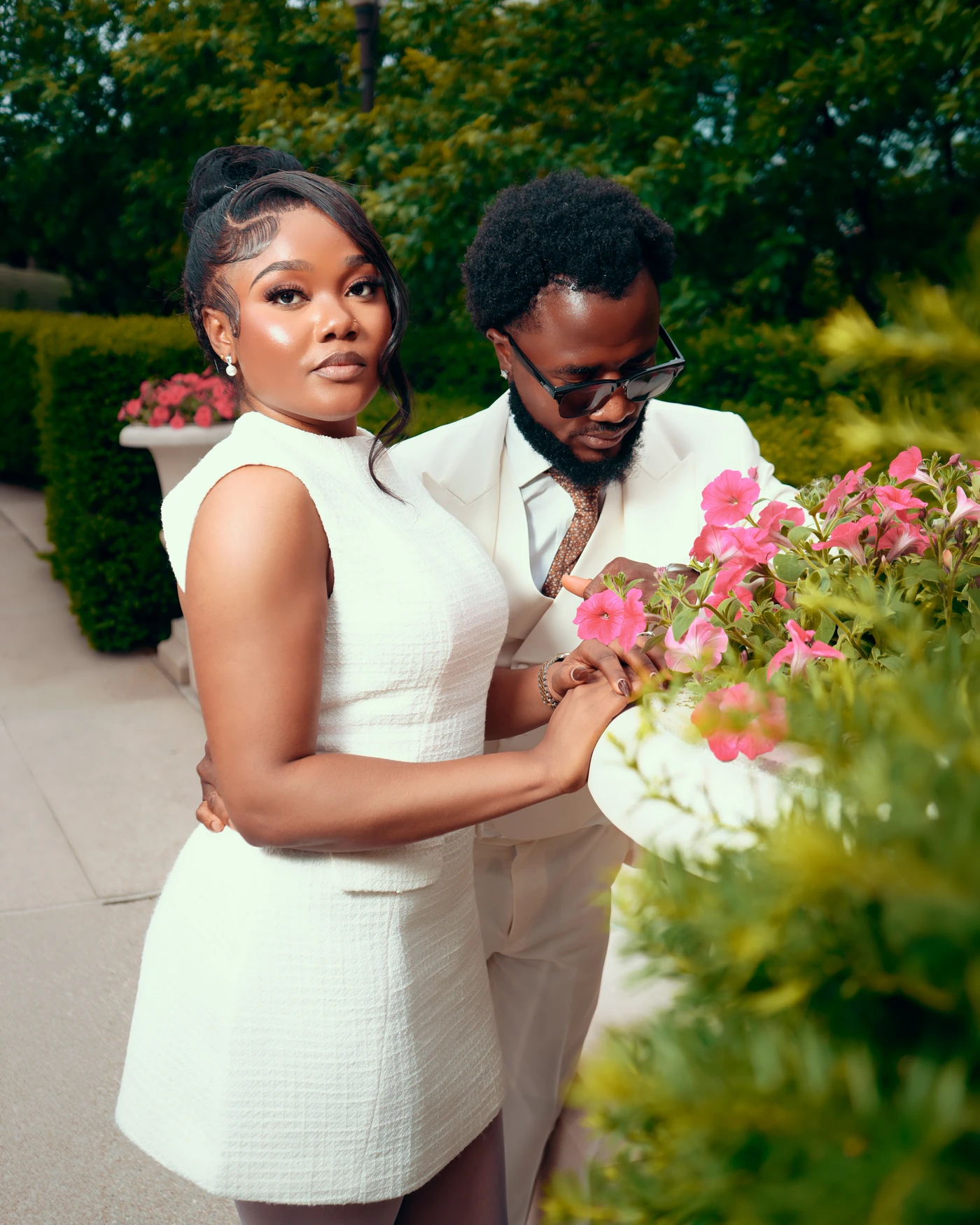 A wedding couple beside pink flowers outdoors